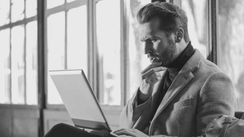 Photo en noir et blanc. Un homme est pensif devant son ordinateur portable. 