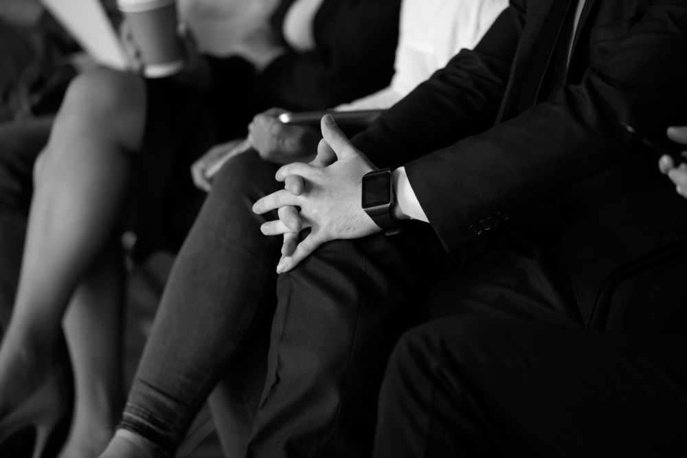 Photo en noir et blanc. Un homme croise les mains sur son genoux. 